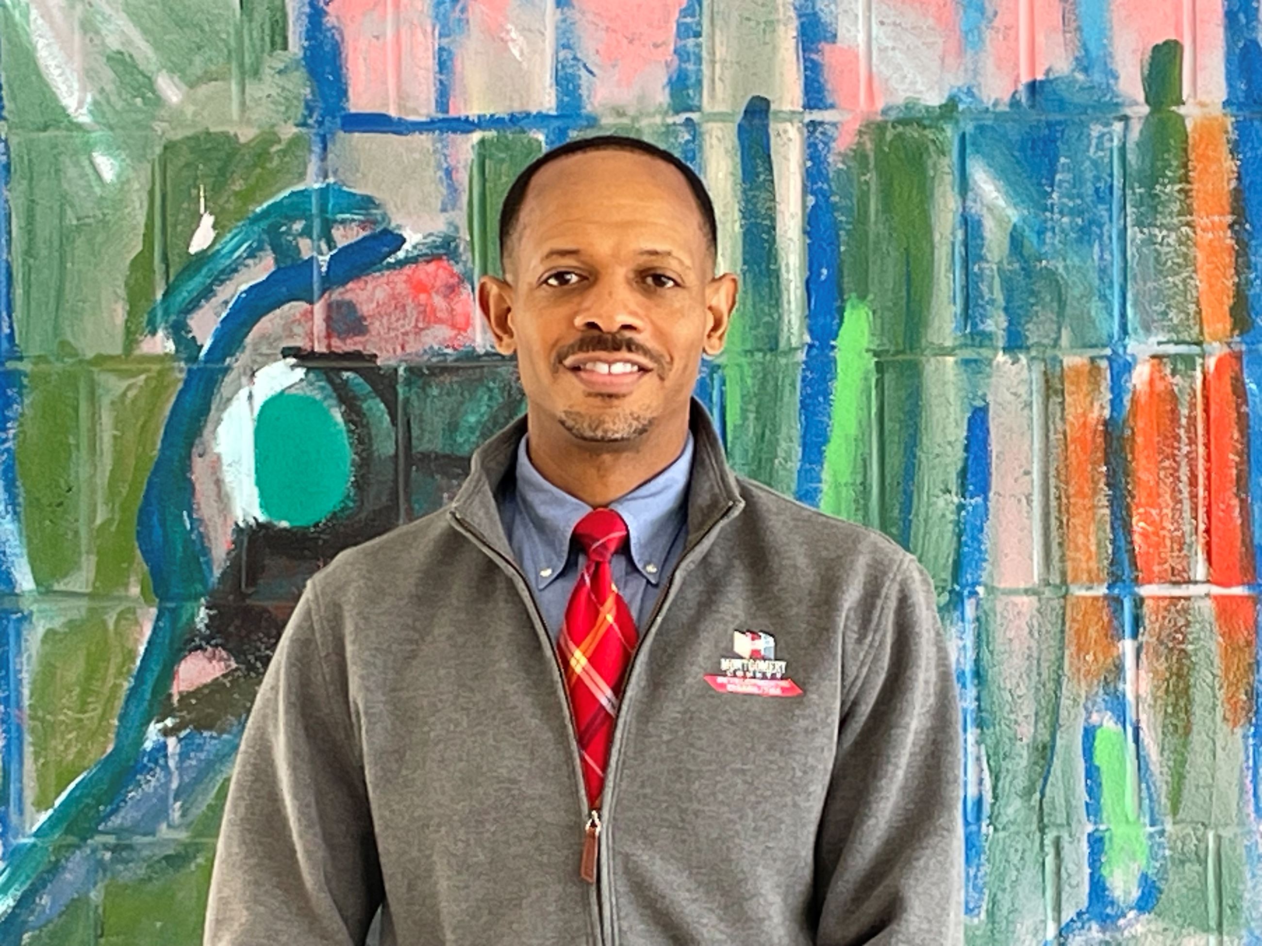 MCBDDS Superintendent Kamarr Gage smiles for the camera wearing a gray fleece zip-up with the logo